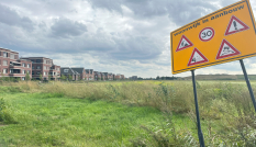 Op de voorgrond een bord met de waarschuwing 'wijk in aanbouw', op de achtergrond een leeg weiland met ernaast een woonwijk