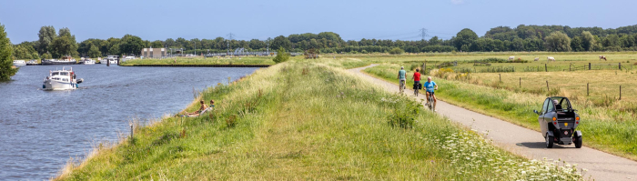 Fietsers en een scootmobieler rijden op een fietspad paralel aan rivier De Eem.